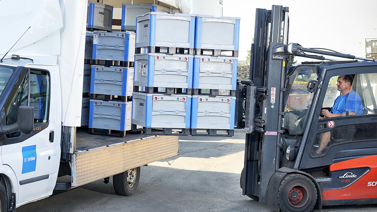 Ein Arbeiter ladet mit Hilfe eines Flurförderzeuges Schwerlastbehälter SL mit Kufen in einen Transporter
