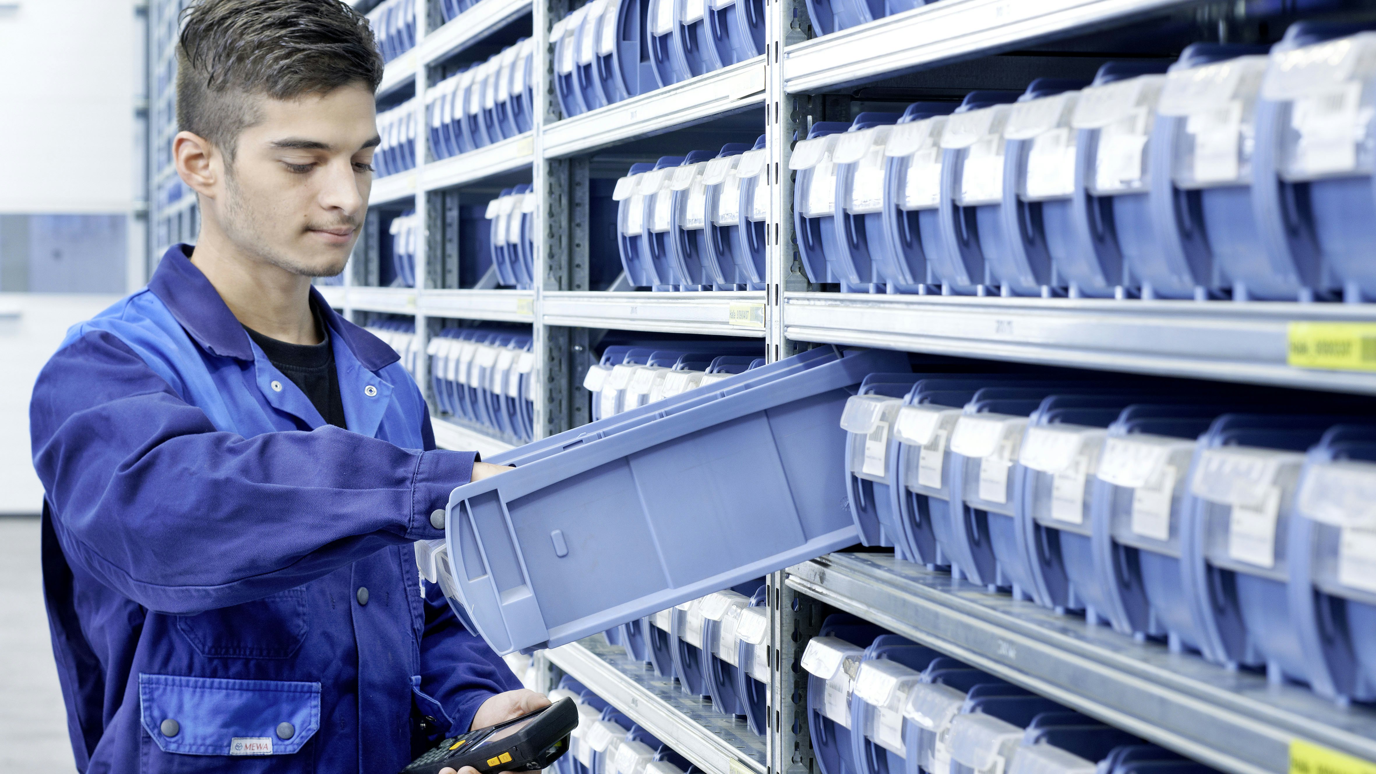 Ein Mitarbeiter entnimmt Ware aus einem Kleinteilebehälter der in einem Fachbodenregal steht