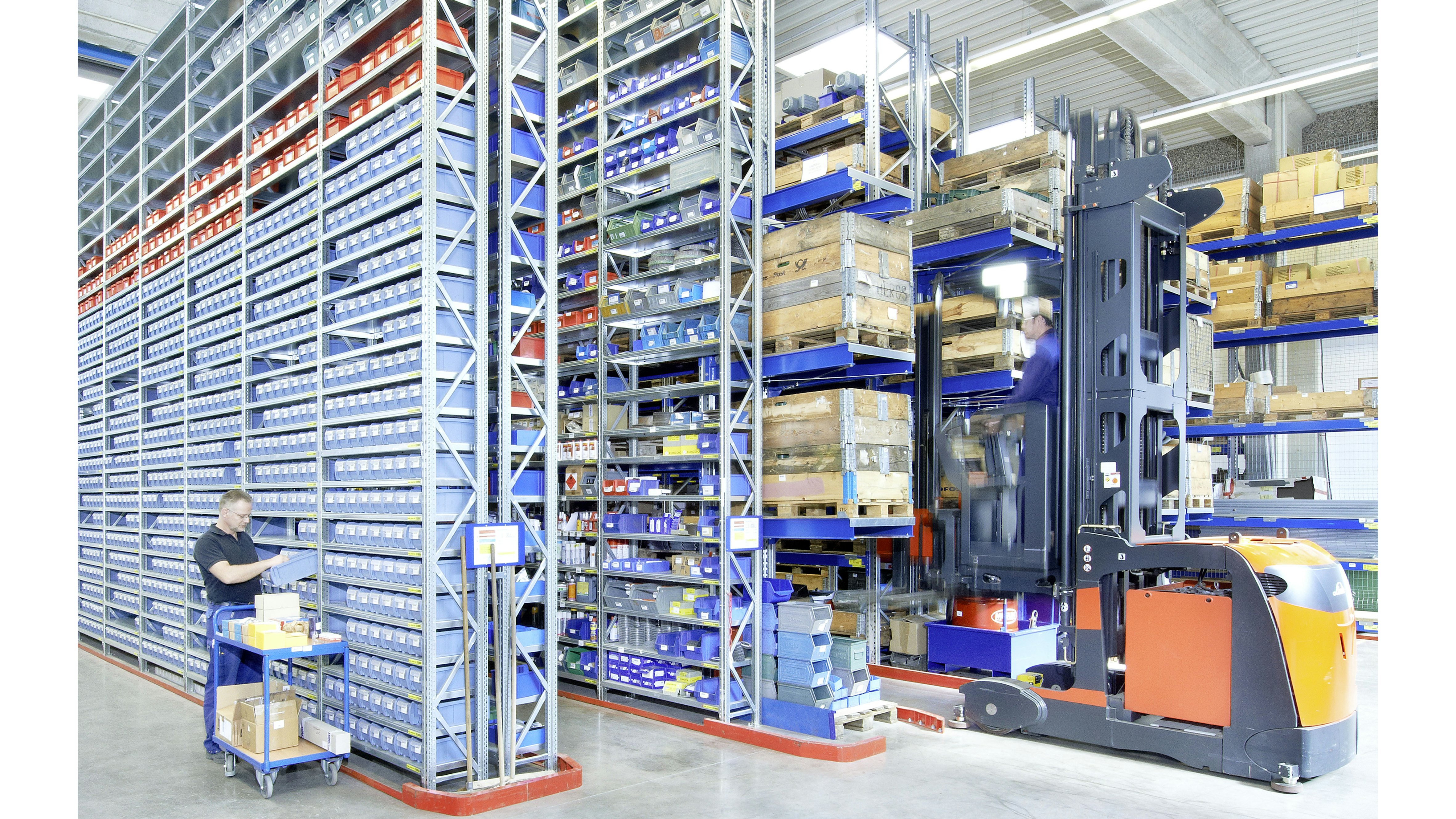 Ein Mitarbeiter entnimmt Ware aus einem Kleinteilebehälter der in einem Fachbodenregal steht