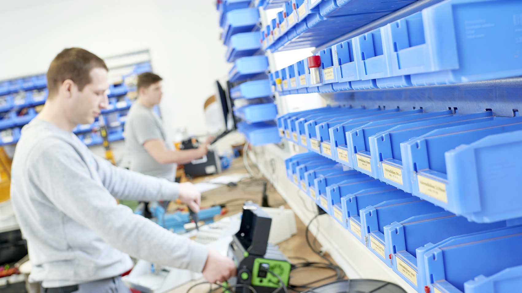 Ein Arbeiter entnimmt Ware aus einem Kleinteilelager, während nein Kollege etwas kontrolliert