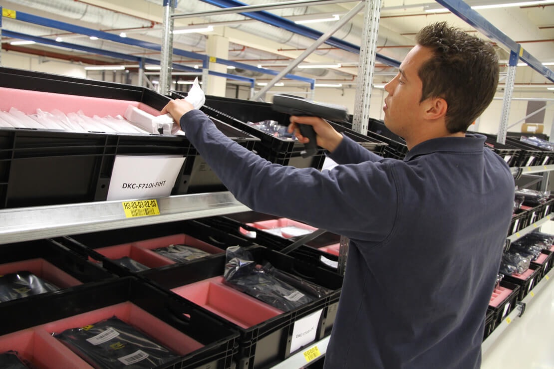 Ihanteellinen herkille elektroniikkakomponenteille Ein Mann scannt ein Produkt aus einem BITO Behälter, der in einem BITO Regal steht, ab.