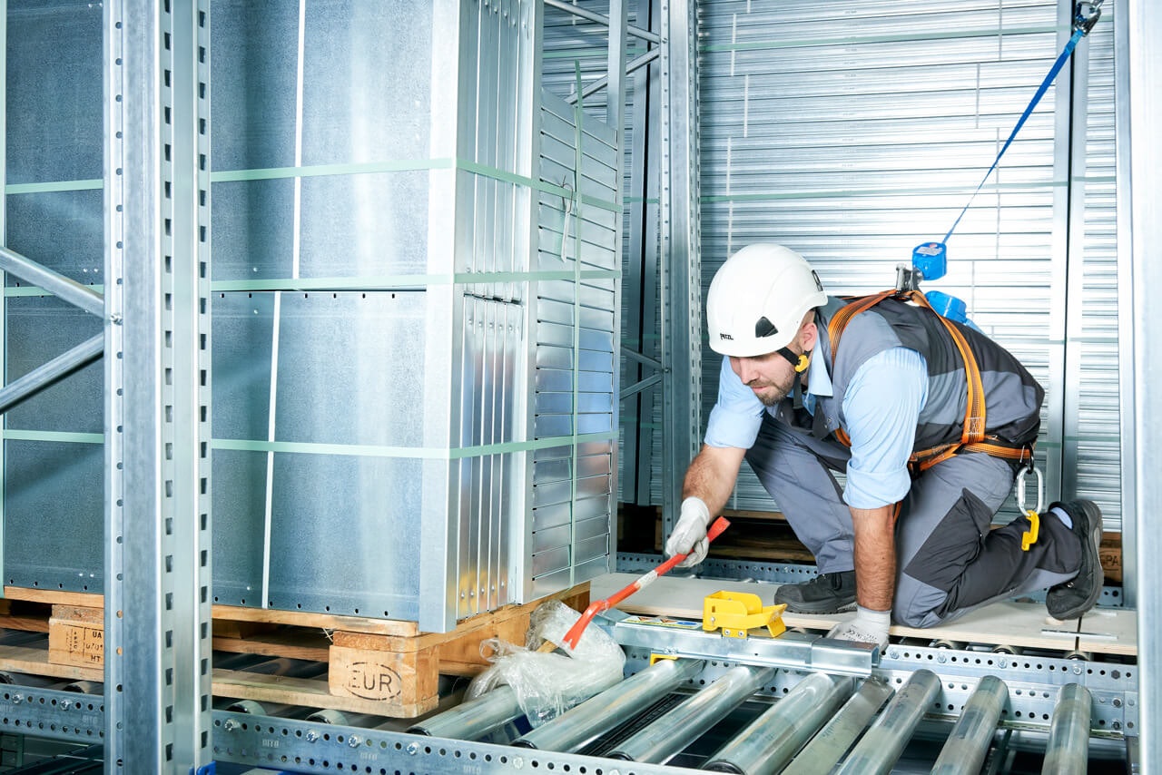 Ein Mitarbeiter mit Schutzausrüstung löst eine Blockade in einem Palettendurchlaufregal
