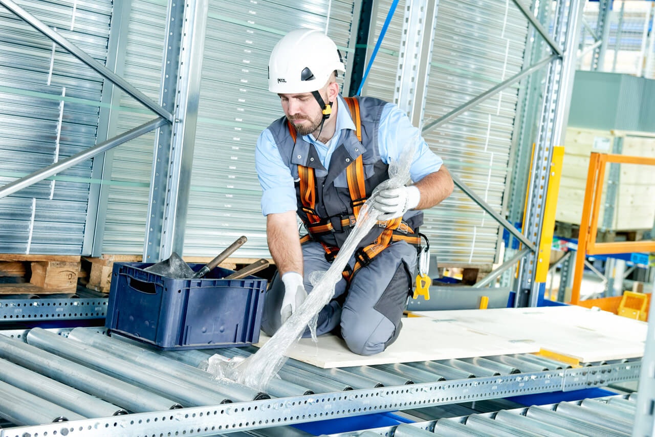Ein Mitarbeiter mit Schutzausrüstung löst eine Blockade in einem Palettendurchlaufregal