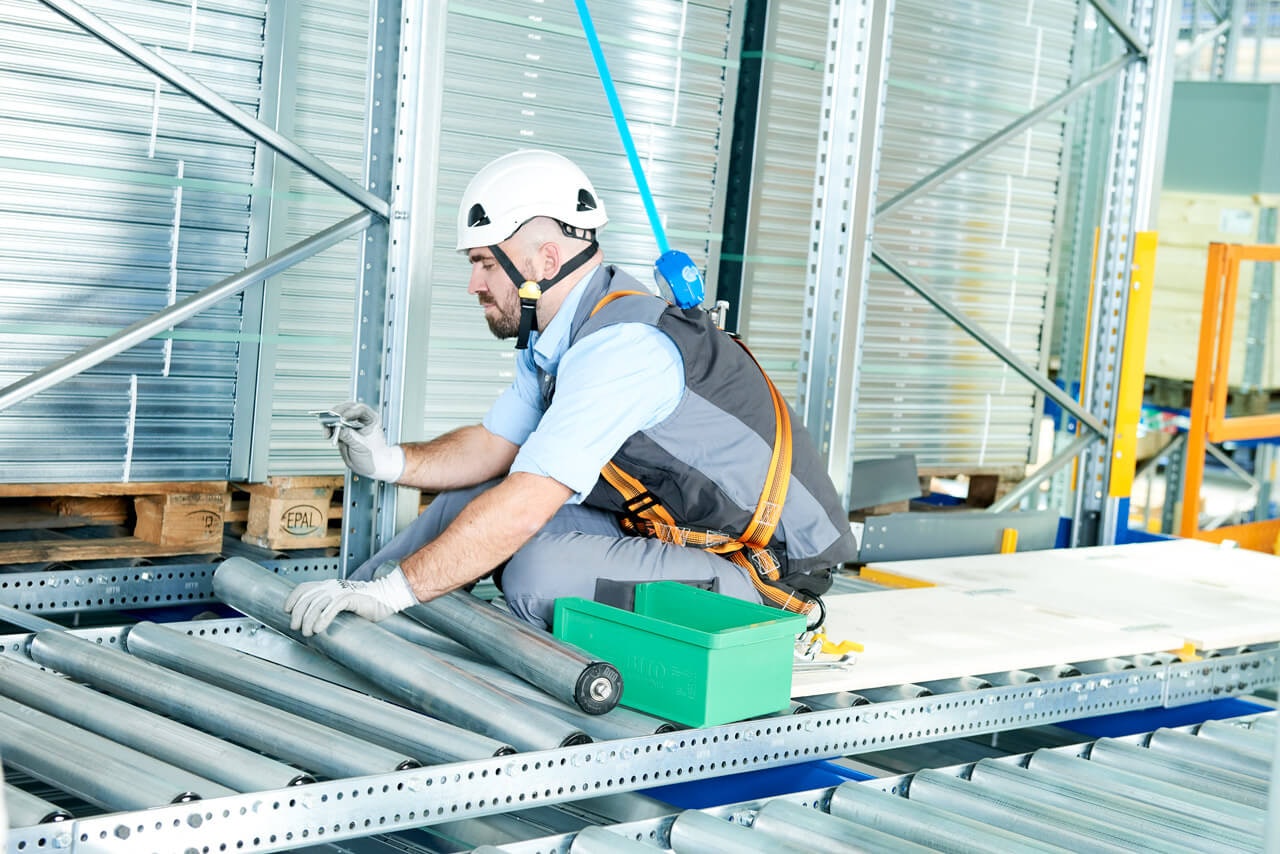 Ein Mitarbeiter mit Schutzausrüstung Rollen in einem Palettendurchlaufregal aus