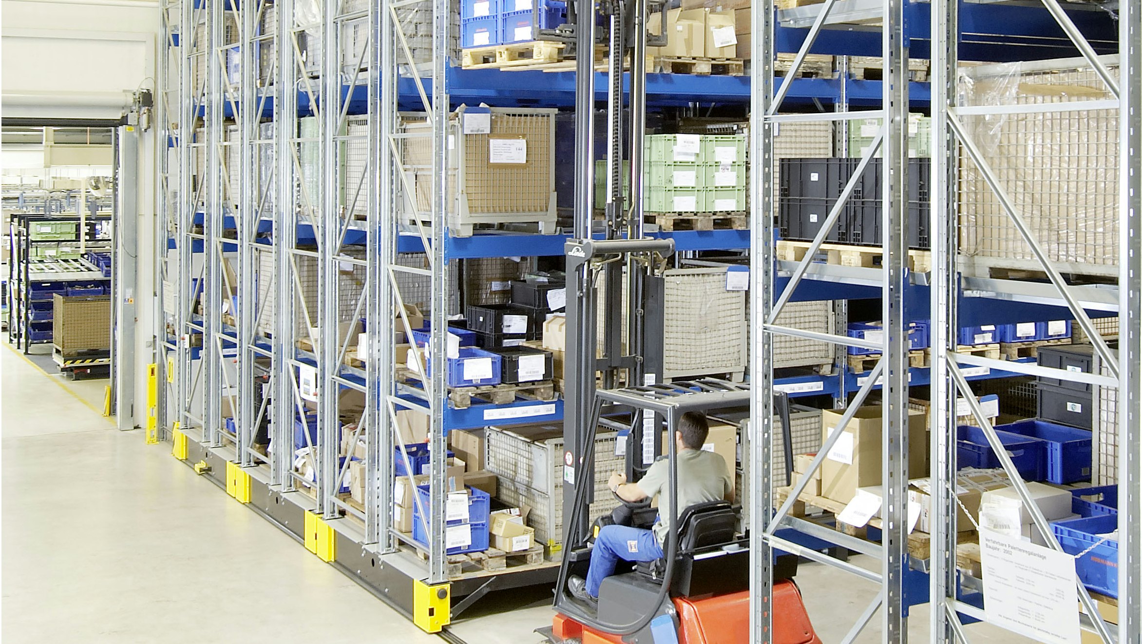 Ein Arbeiter entnimmt, mit Hilfe eines Flurförderzeuges; eine Palette aus einem verfahrbaren Palettenregal