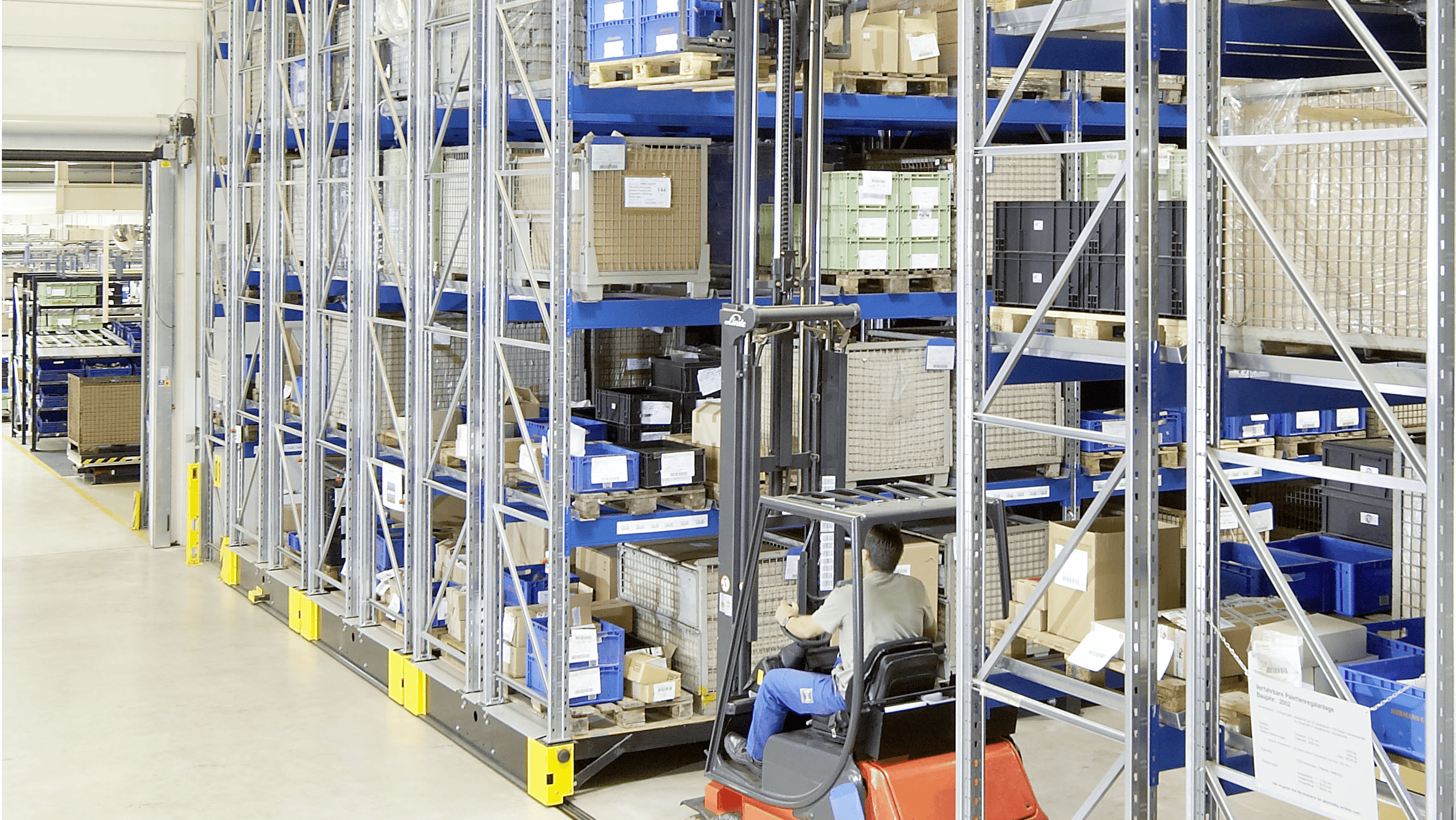 Ein Arbeiter entnimmt, mit Hilfe eines Flurförderzeuges; eine Palette aus einem verfahrbaren Palettenregal