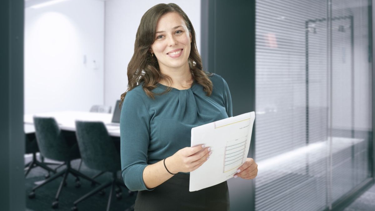 Eine Frau, mit einer Zeichnung in der Hand, vor einem Besprechungsraum.