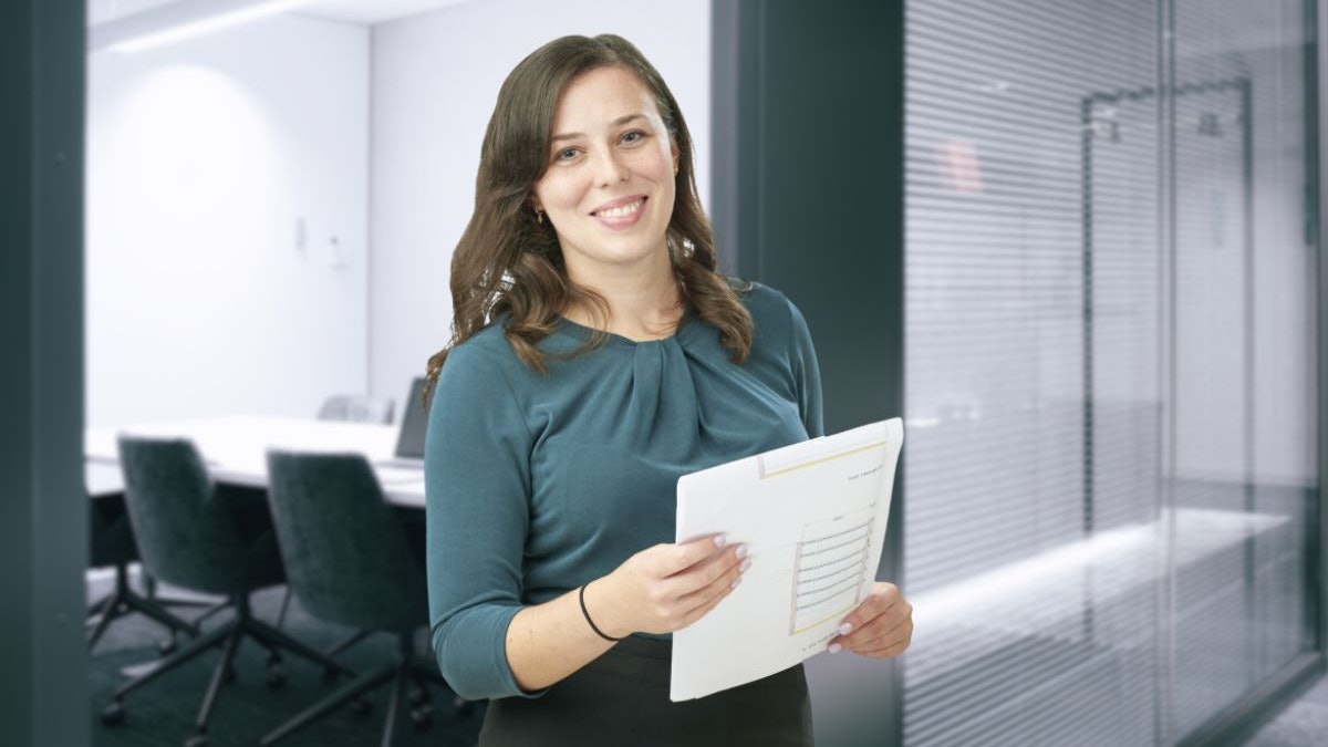 Eine Frau, mit einer Zeichnung in der Hand, vor einem Besprechungsraum.