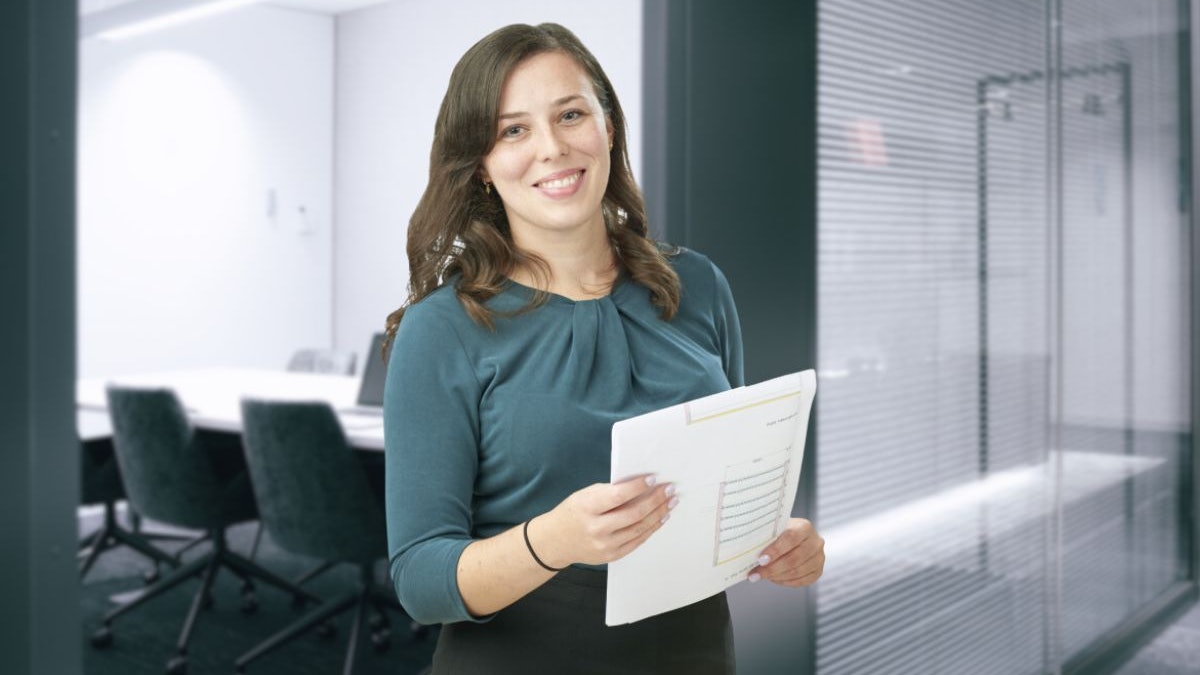 Eine Frau, mit einer Zeichnung in der Hand, vor einem Besprechungsraum.