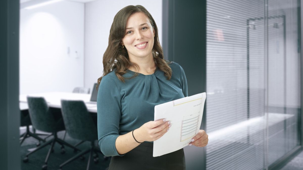 Eine Frau, mit einer Zeichnung in der Hand, vor einem Besprechungsraum.