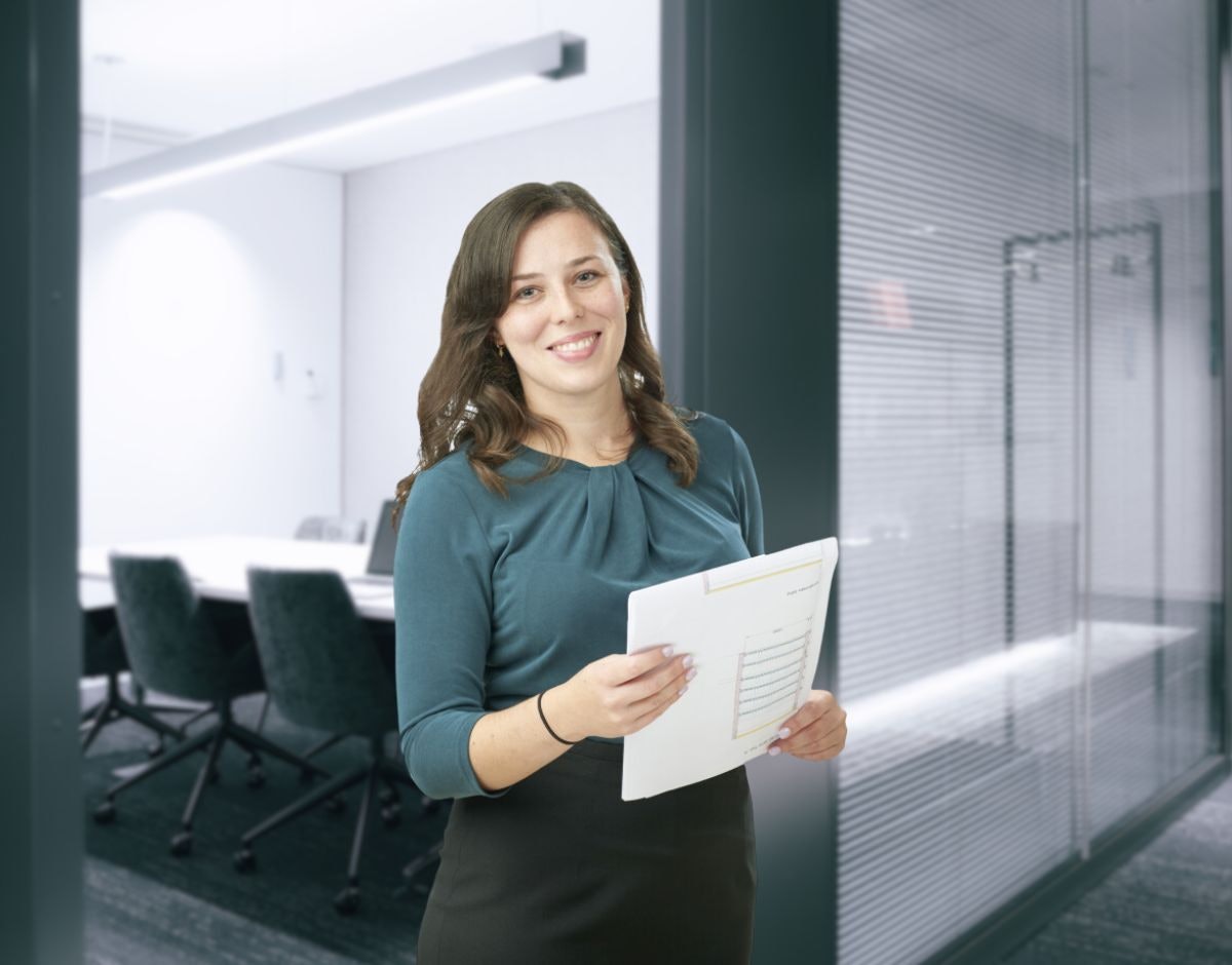 Eine Frau, mit einer Zeichnung in der Hand, vor einem Besprechungsraum.